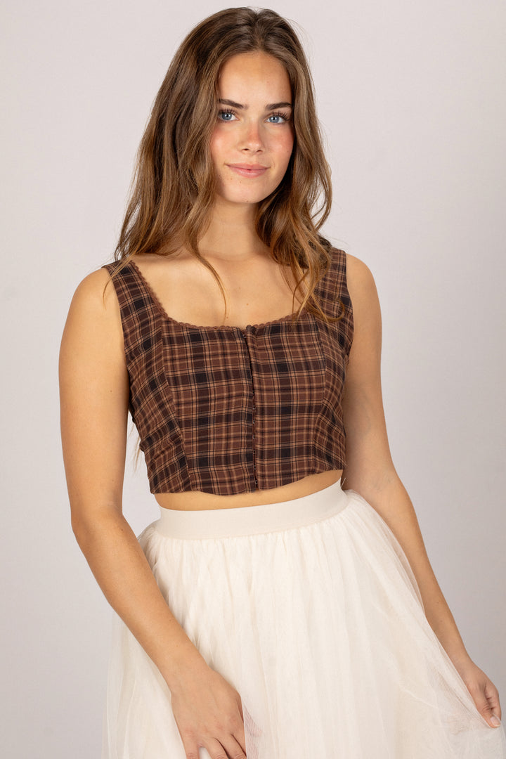A young woman with long brown hair wearing a plaid cropped top and a white tulle skirt.