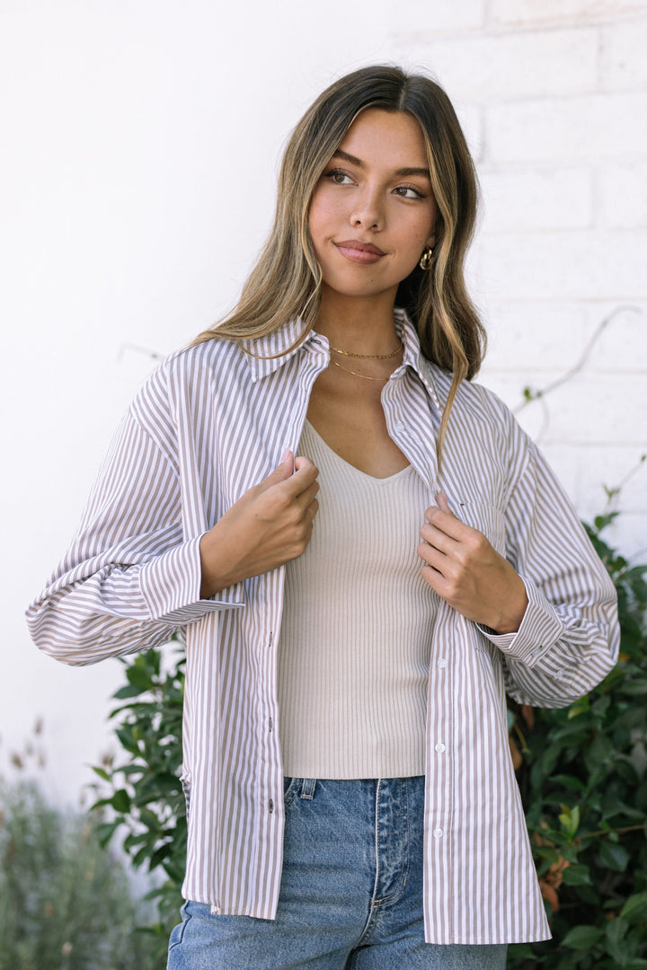 A young woman models a striped button-up shirt in a light pink and white color scheme with a relaxed, feminine fit.