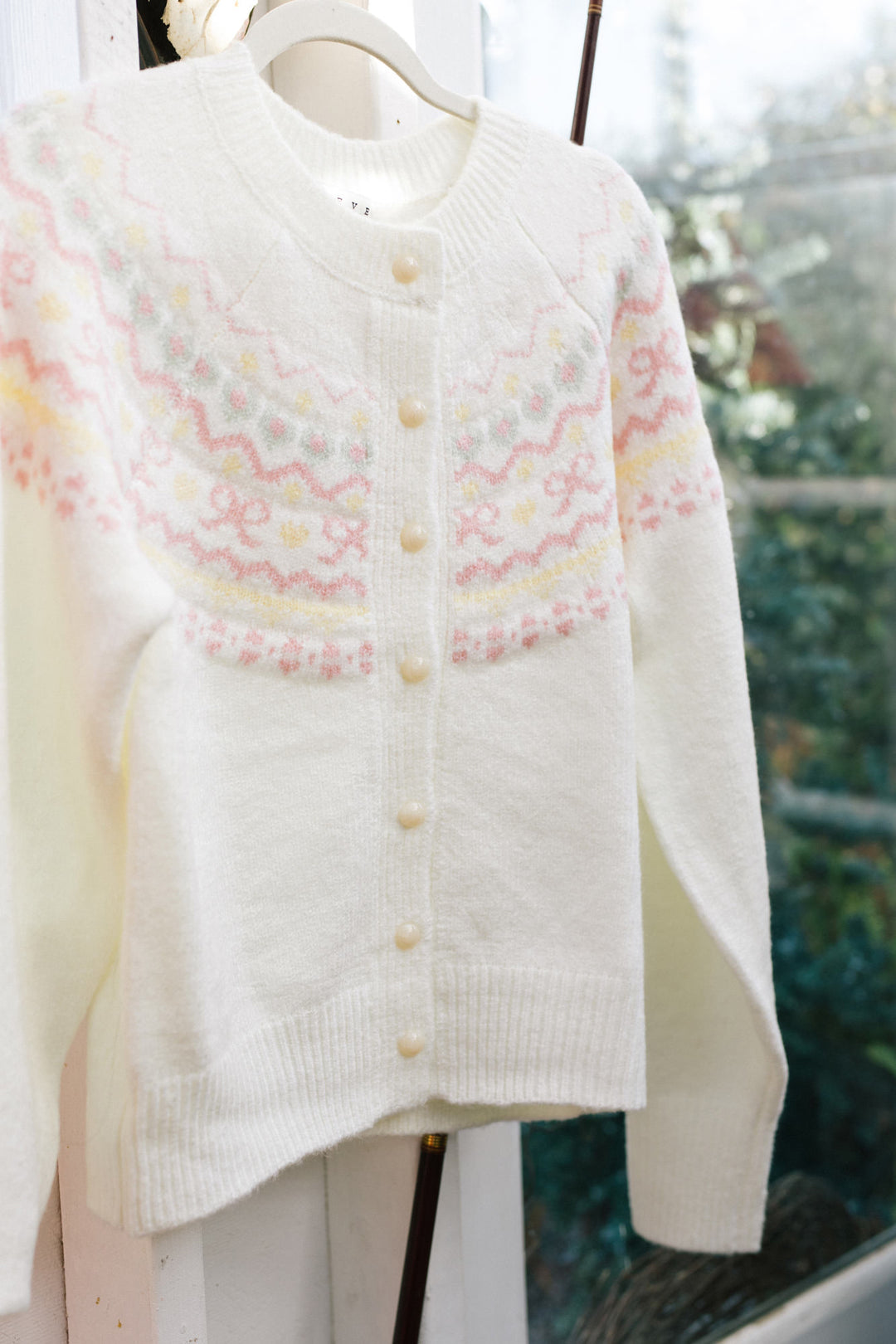 A white knitted cardigan with a textured floral pattern, featuring a high collar, buttons, and a relaxed, oversized fit.