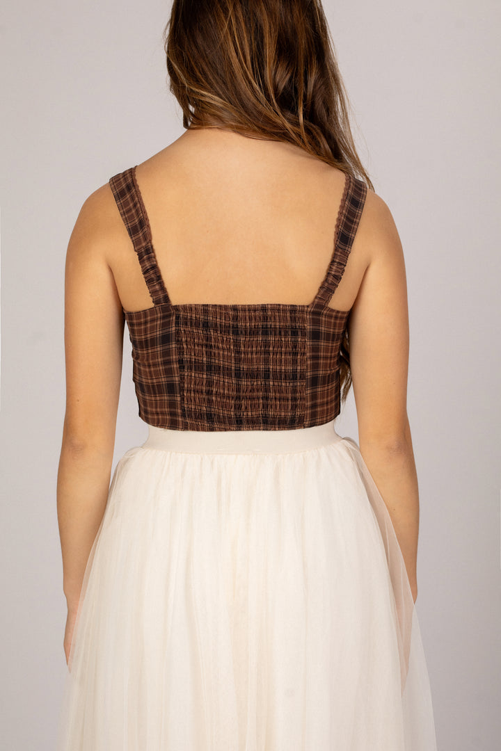 A brown plaid cropped tank top with adjustable spaghetti straps and a smocked bodice, paired with a flowy white midi skirt.