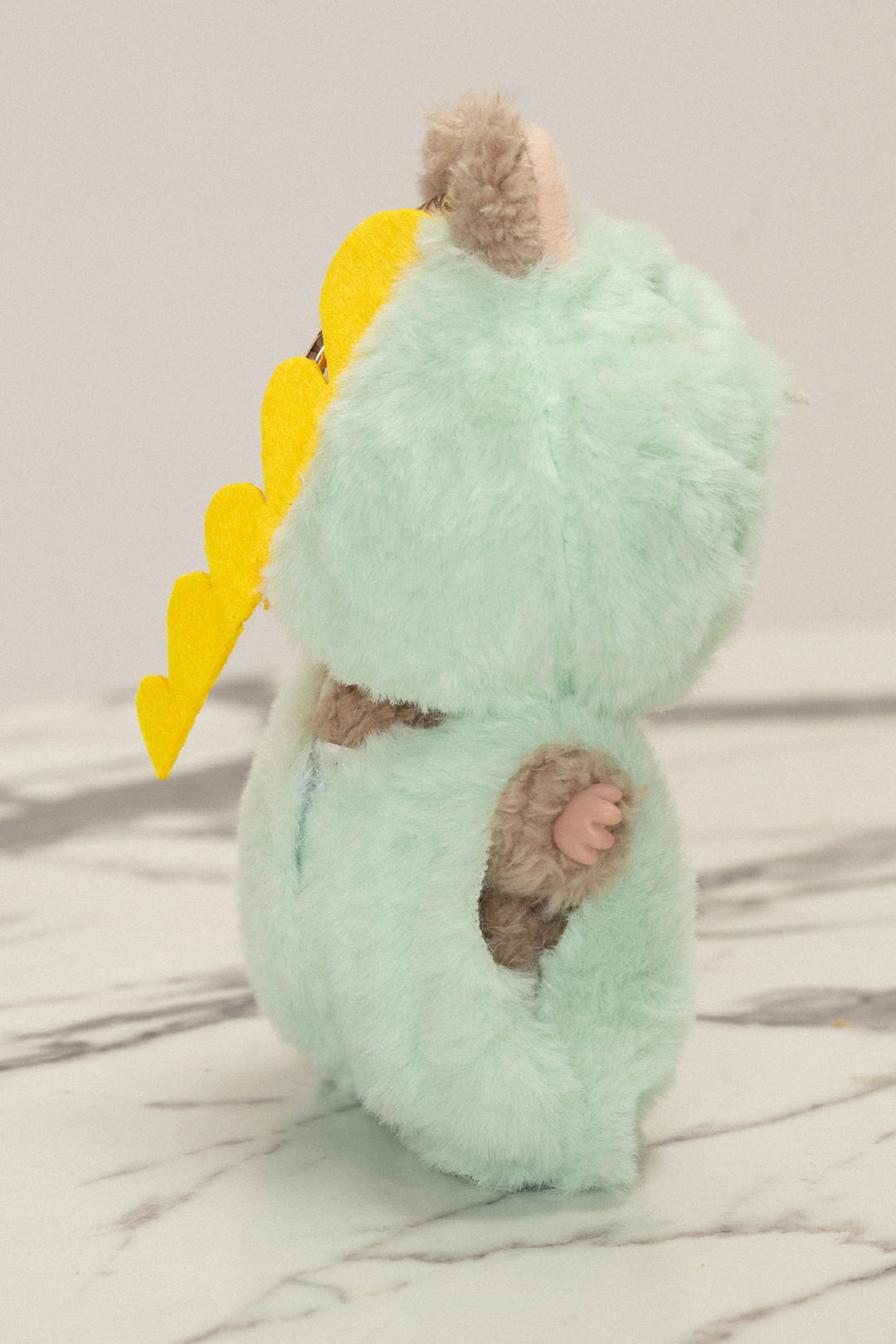 Plush mint green dinosaur-inspired toy with brown fur accents and yellow horns or spikes.