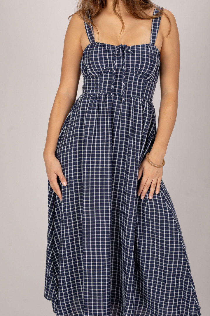 A navy and white plaid midi dress with a smocked bodice, adjustable straps, and a flowy skirt.
