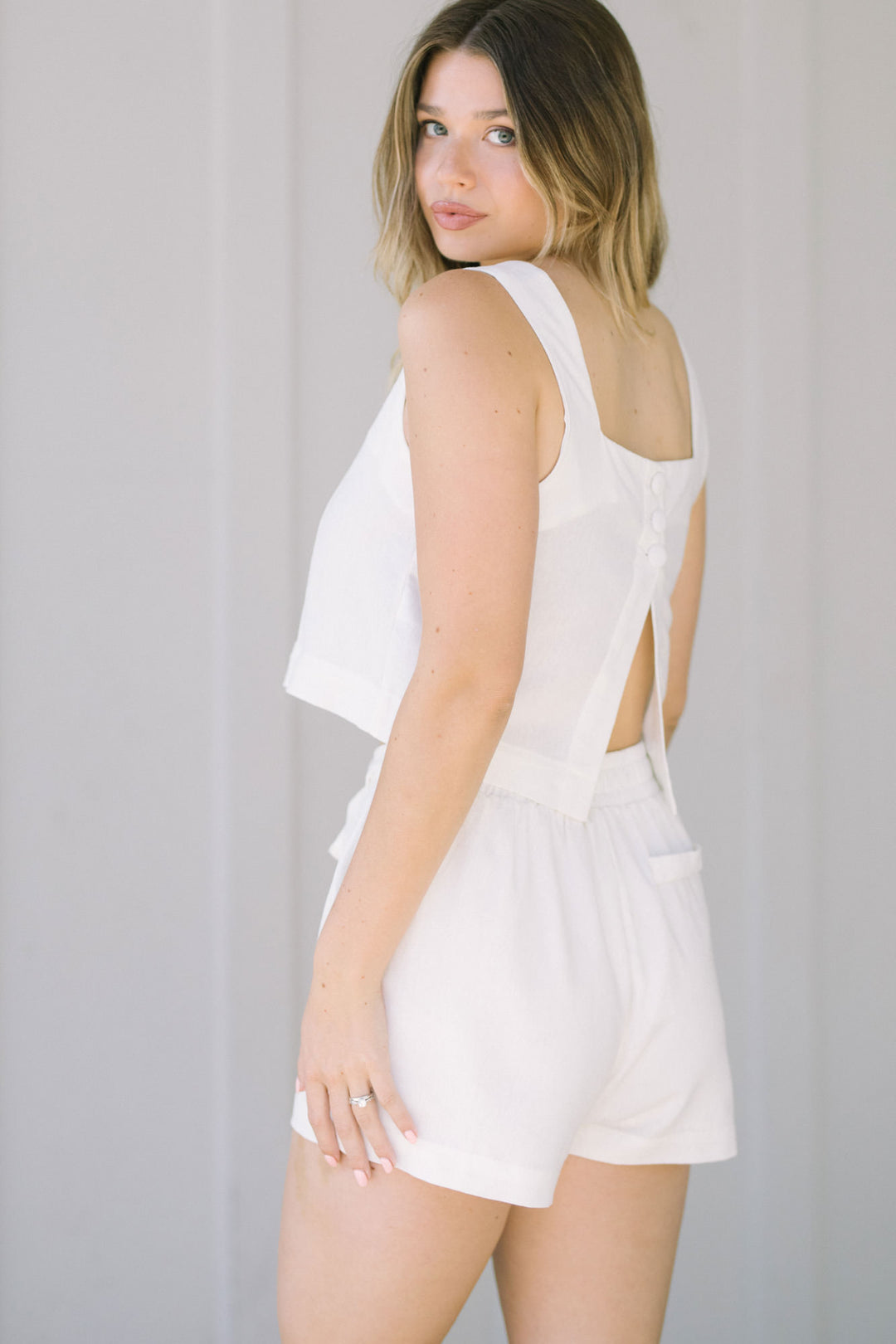 White high-waisted shorts with a waist tie detail, featuring a ruffled hem and a clean, minimalist design.
