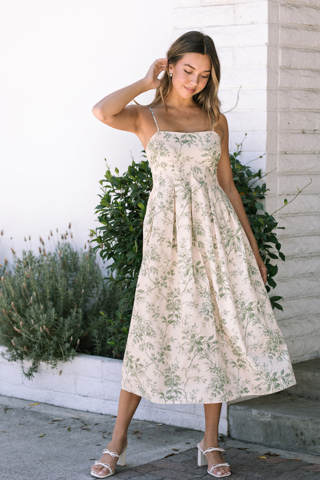 A floral midi dress with spaghetti straps, featuring a flowing silhouette and a white background with lush greenery.