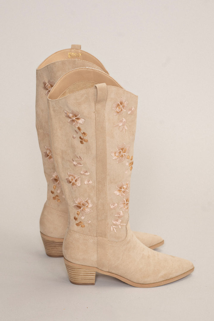 Pair of tan suede cowboy boots with embroidered floral details and stacked heels.