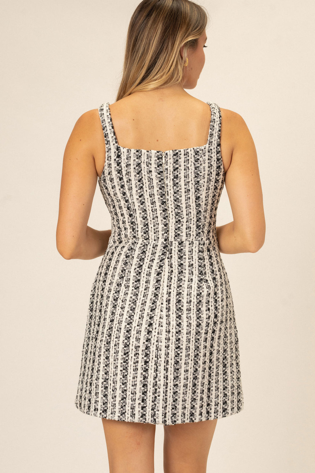 Sleeveless A-line mini dress in a monochrome tweed pattern, featuring a fitted bodice and flowy skirt.