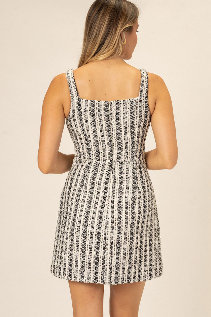 Sleeveless A-line mini dress in a monochrome tweed pattern, featuring a fitted bodice and flowy skirt.