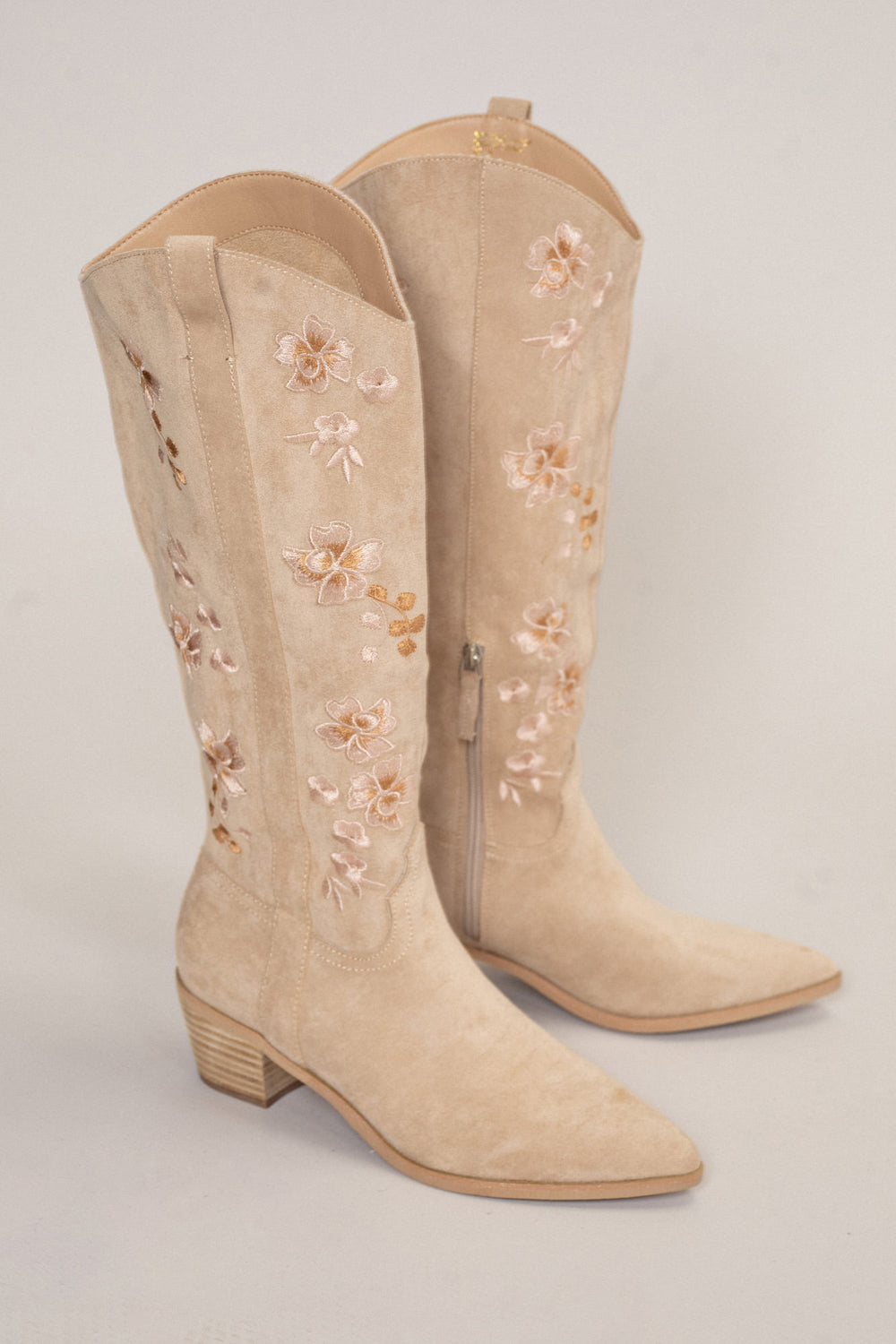 Beige suede cowboy boots with delicate floral embroidery and a low block heel.