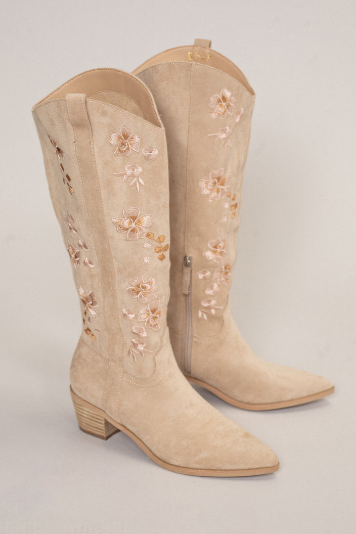 Beige suede cowboy boots with delicate floral embroidery and a low block heel.
