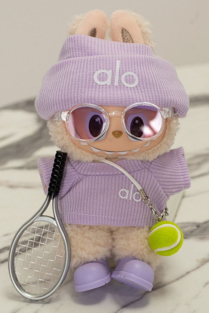 Plush tennis-themed stuffed animal wearing a lavender outfit with Alo logo, holding a tennis racket and ball.
