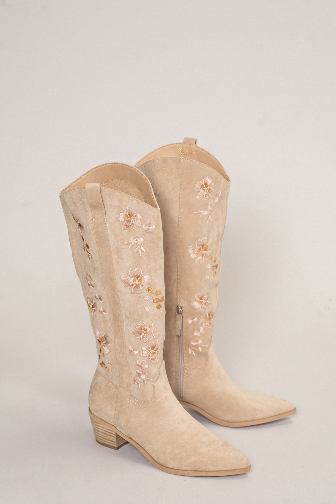Pair of tan suede cowgirl boots with delicate floral embroidery and a pointed toe.