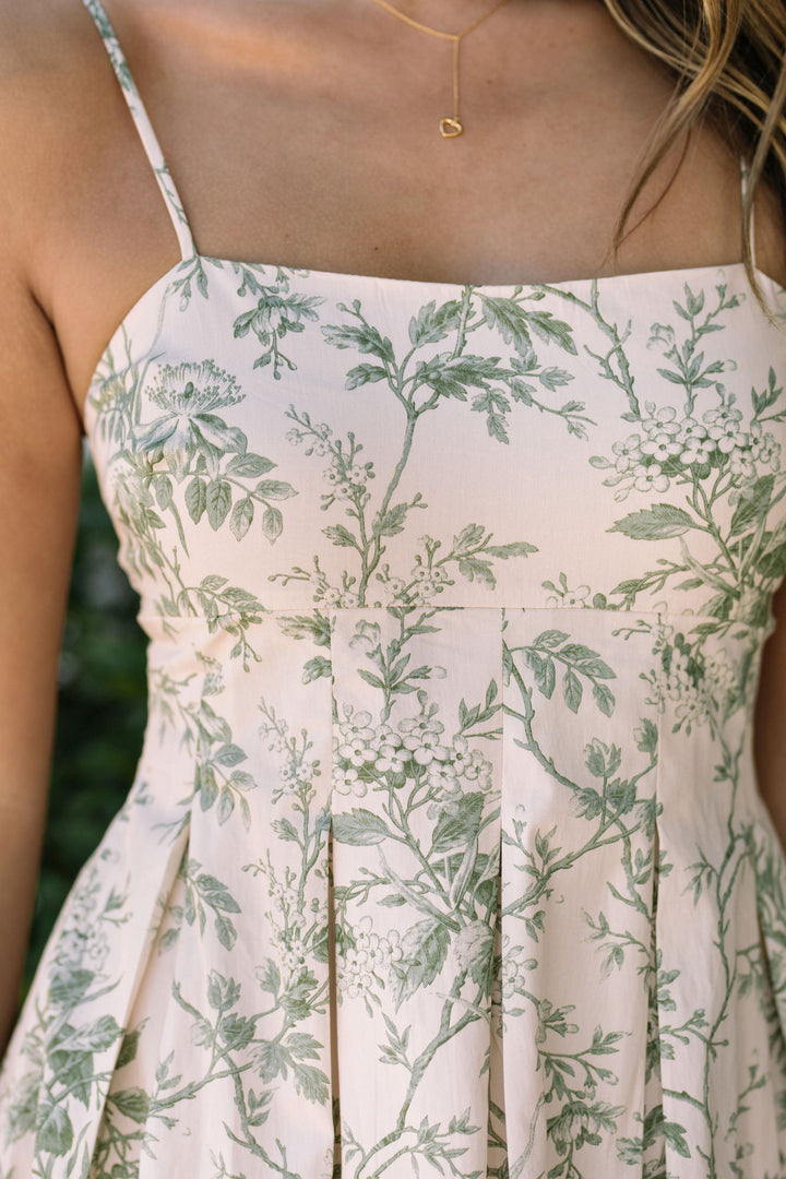 A delicate white dress featuring a flowing floral print in shades of green, with a spaghetti-strap bodice and a midi-length skirt.