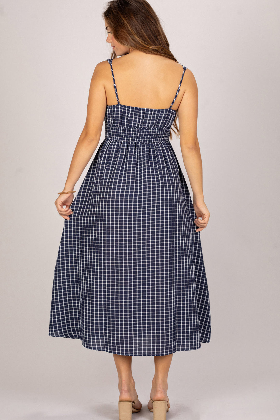 A navy and white checkered midi dress with spaghetti straps and a smocked waist, creating a flattering and feminine silhouette.