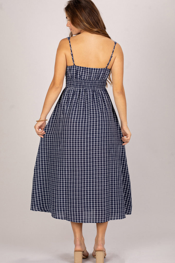 A navy and white checkered midi dress with spaghetti straps and a smocked waist, creating a flattering and feminine silhouette.