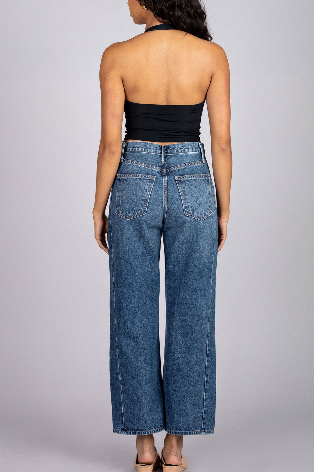 A black halter-style crop top with a sleek, fitted silhouette, showcased on a model with long, dark hair facing away from the camera.