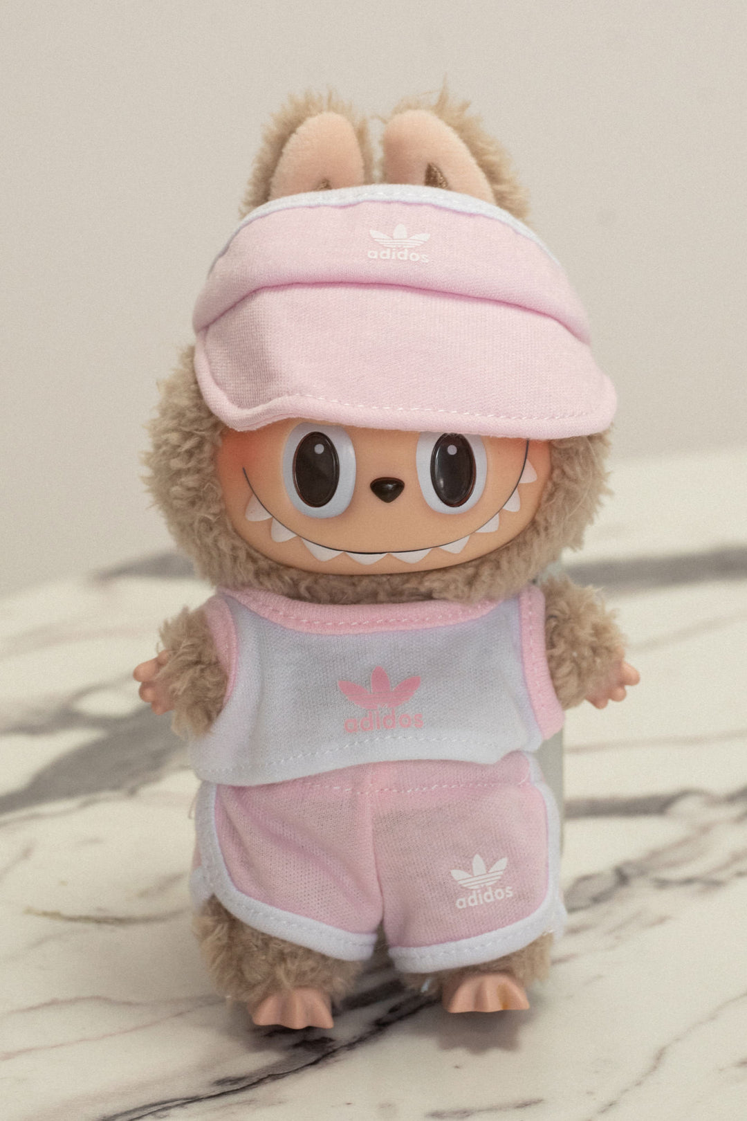 A plush, gray and pink stuffed animal wearing an Adidas visor, tank top, and shorts with the Adidas logo.