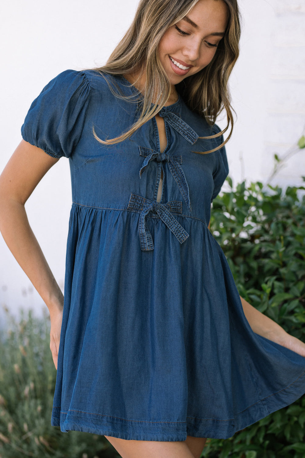 A blue denim mini dress with puffed sleeves, tie details, and a flared, high-waisted silhouette.