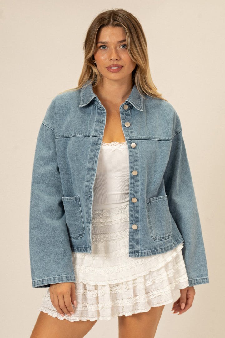 A light blue denim jacket with front buttons, chest pockets, and a relaxed, casual style.