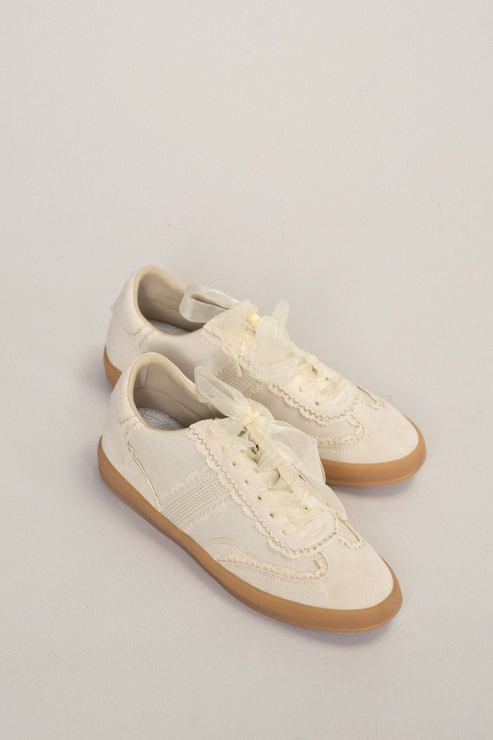 Cream-colored sneakers with lace detailing and tulle accents on the uppers, featuring a gum rubber sole.