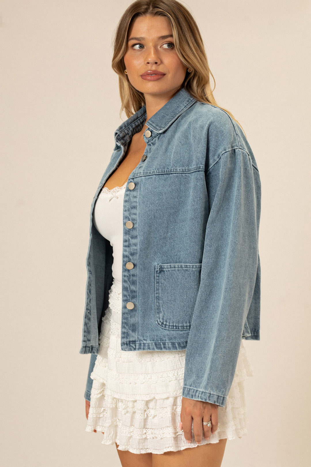 A woman wearing a blue denim jacket with button front closure, featuring a relaxed, oversized fit.