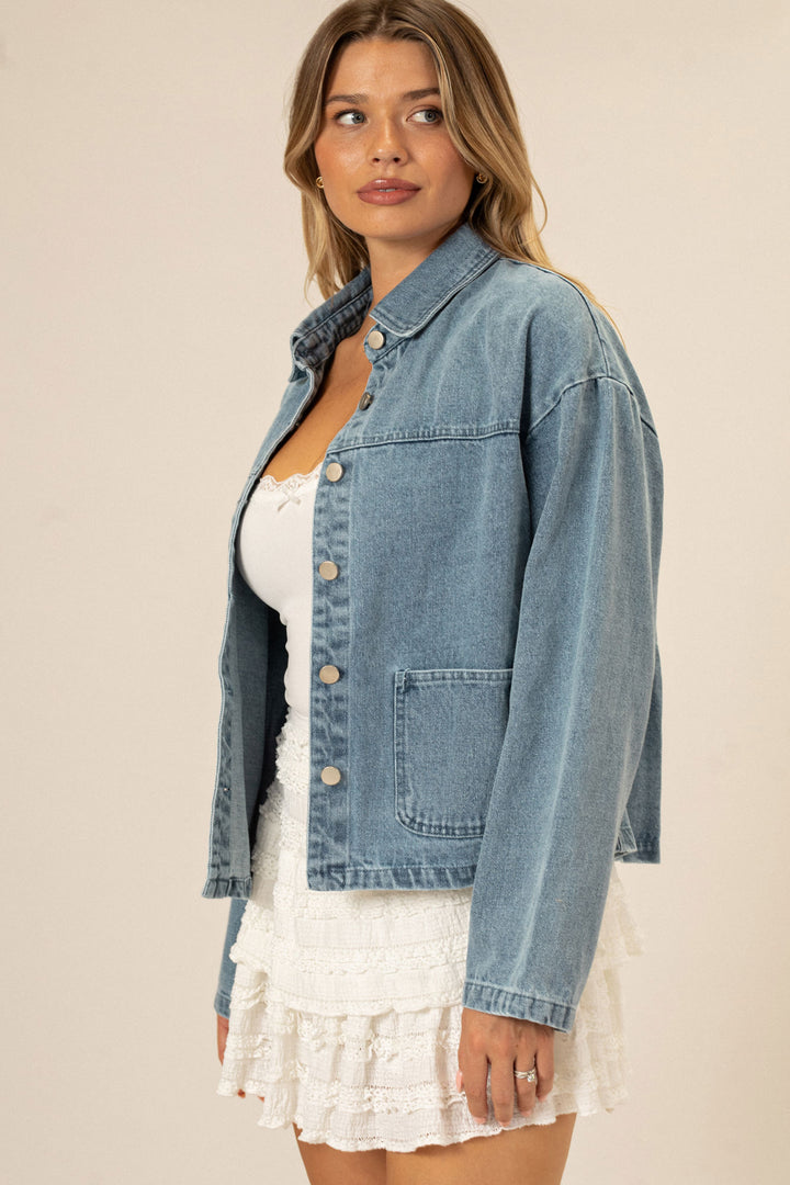 A woman wearing a blue denim jacket with button front closure, featuring a relaxed, oversized fit.