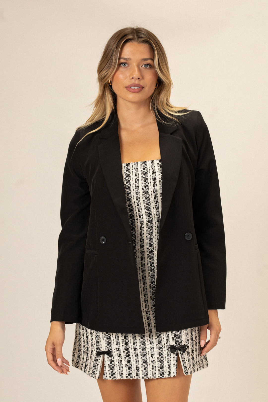 A woman in a black double-breasted blazer over a patterned mini dress, with long blonde wavy hair.