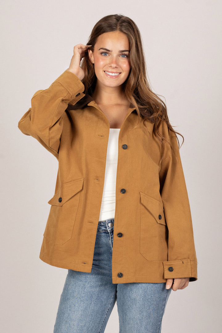 A woman wearing a mustard-colored, oversized barn jacket with button-up front, two front pockets, and long sleeves.