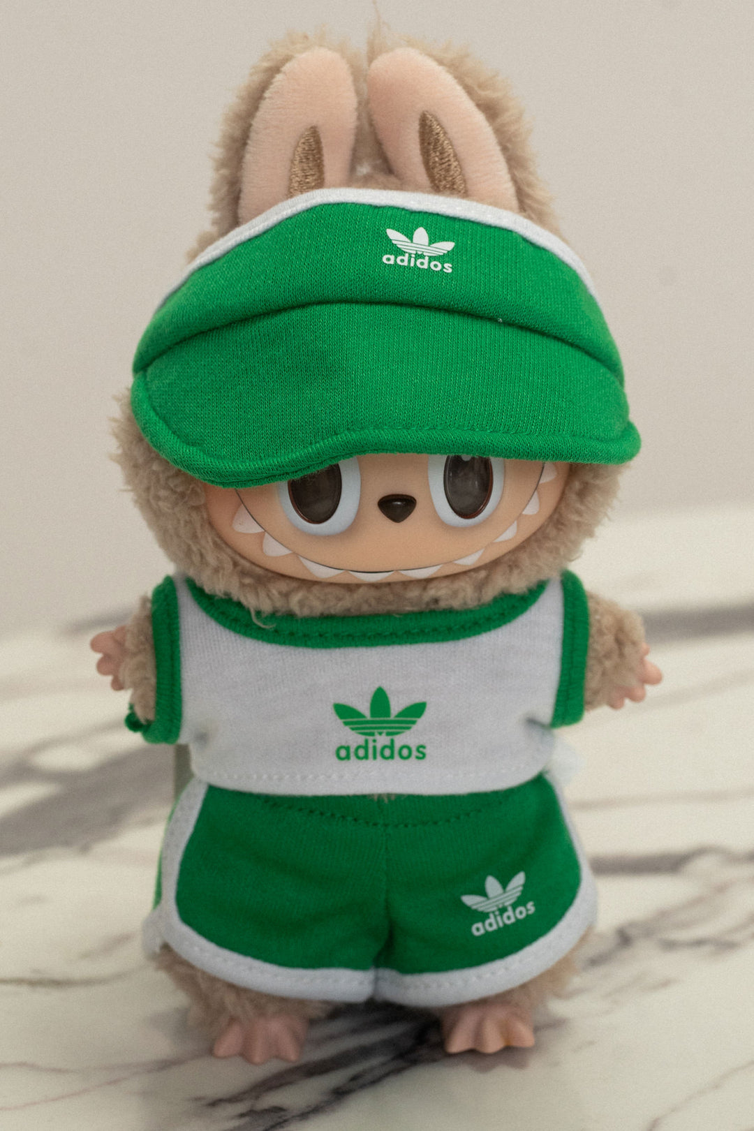 Plush toy wearing Adidas green visor, shorts, and shirt with Adidas logo