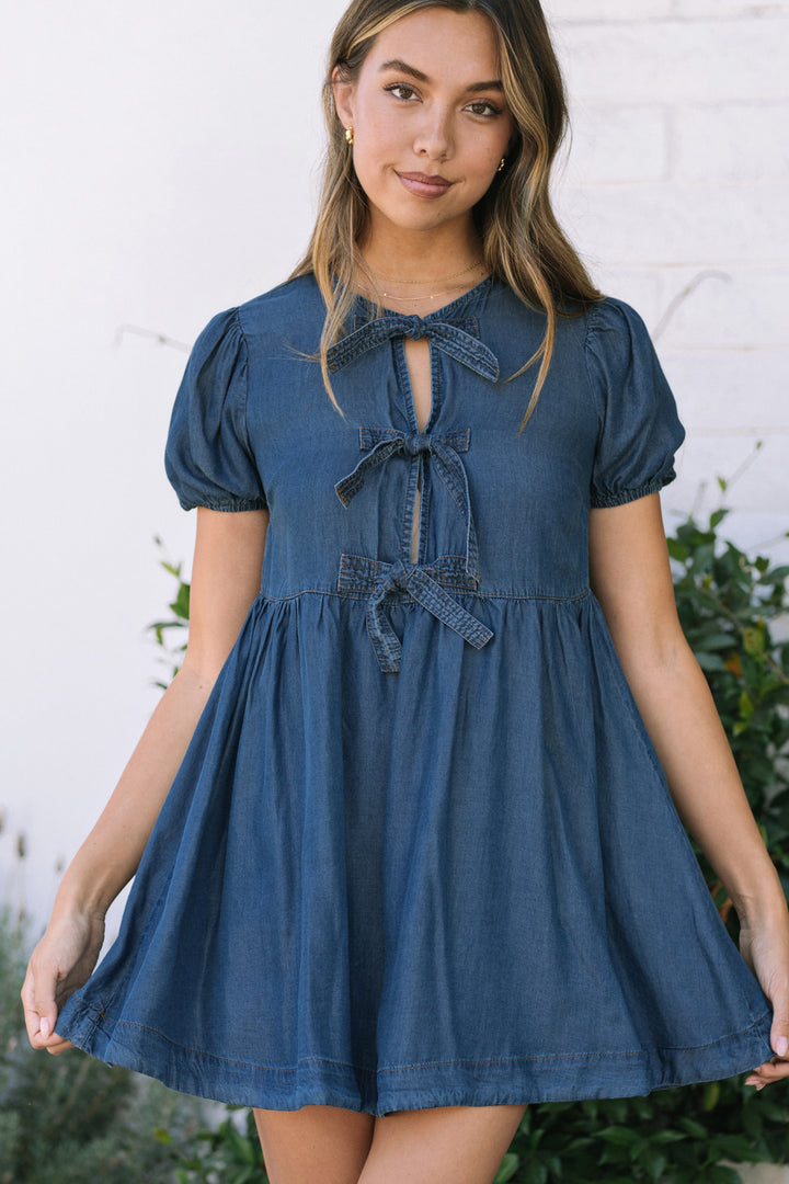 Denim mini dress with puff sleeves, tie front, and flared skirt in a dark wash blue color.