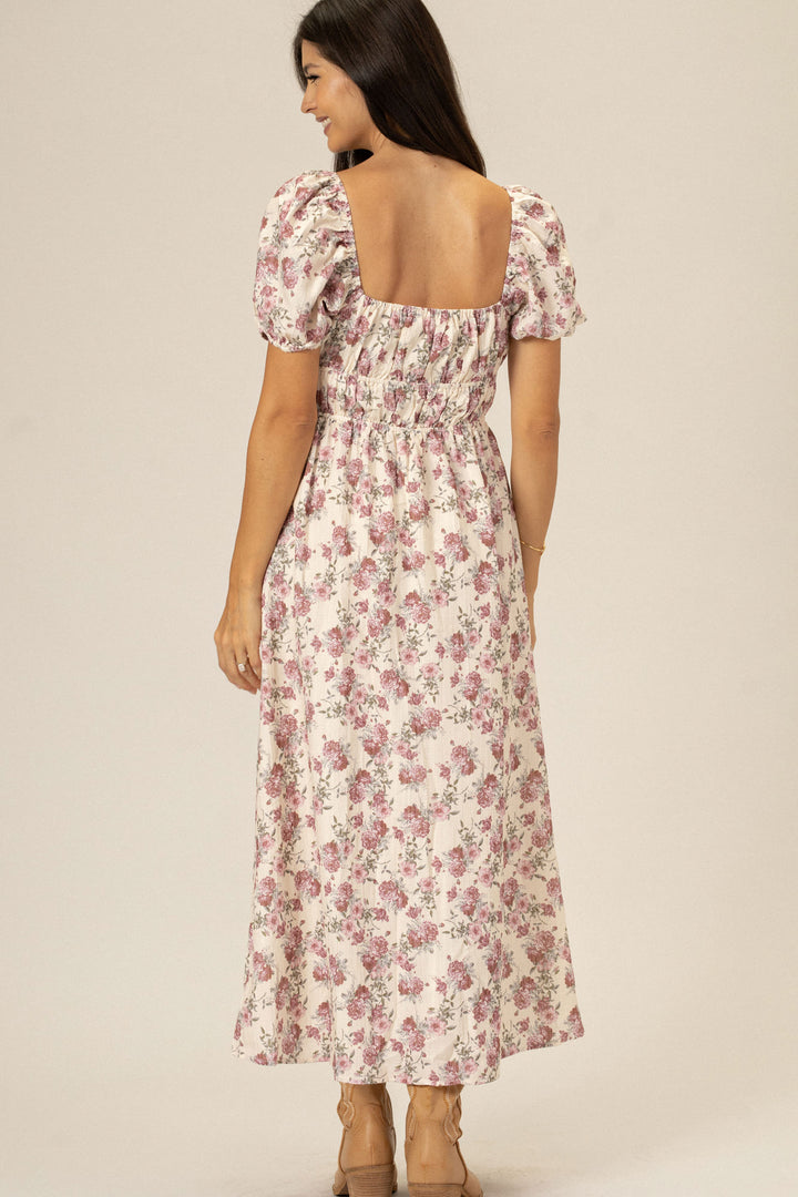 A floral print dress with puff sleeves, a square neckline, and a tiered, flowing skirt, in a soft pink and white color palette.