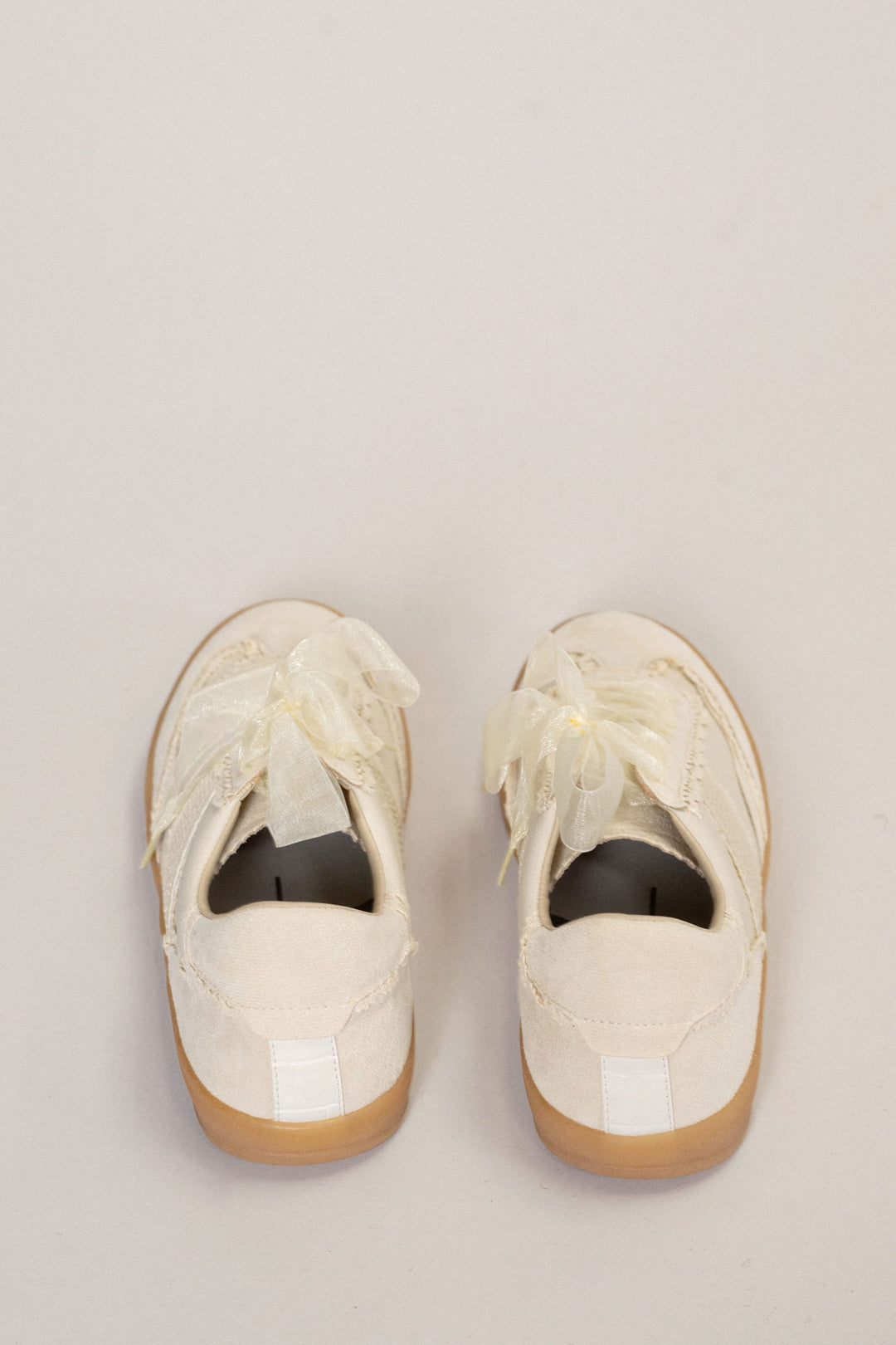 Pair of white sneakers with lace and tulle accents, featuring a gum sole for a retro, casual look.