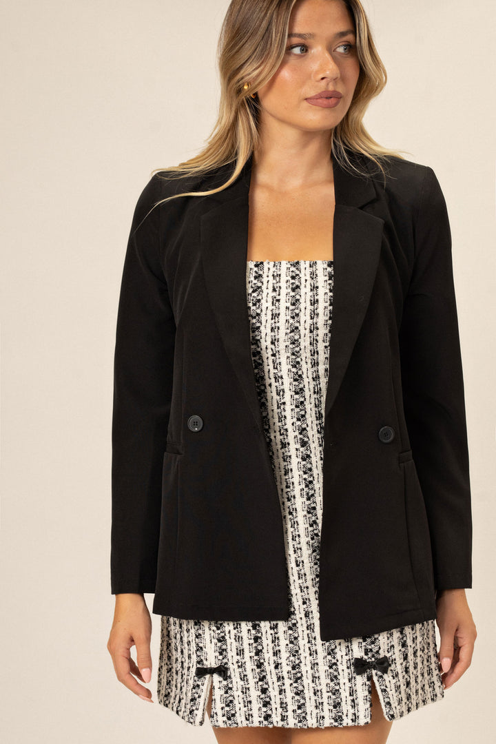 A black, double-breasted blazer with a slim, tailored silhouette, featuring a flattering neckline and structured shoulders on a waist-length model.
