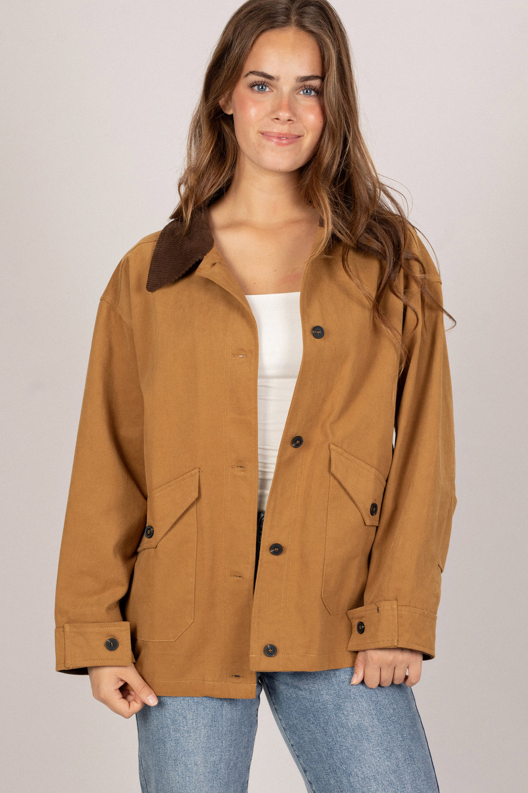 A woman wearing a tan, oversized barn jacket with a collared neckline and front button closure.