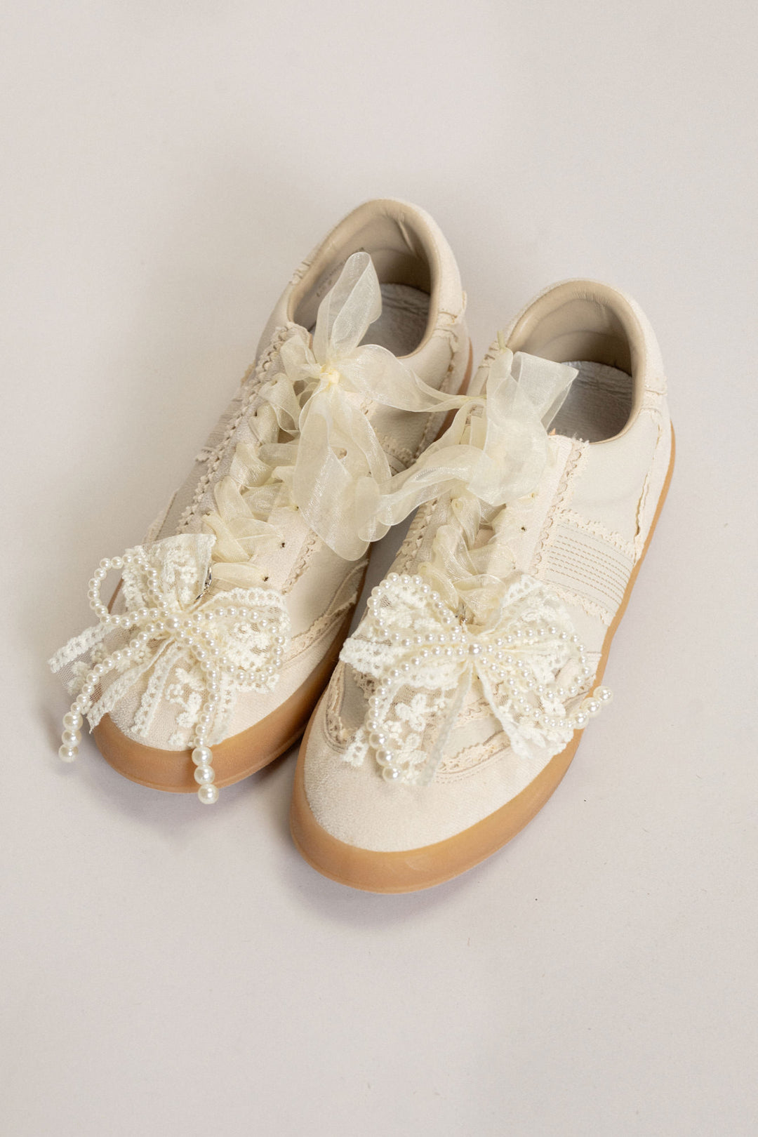 Ivory lace and tulle adorned sneakers with pearl accents and lace-up closure.