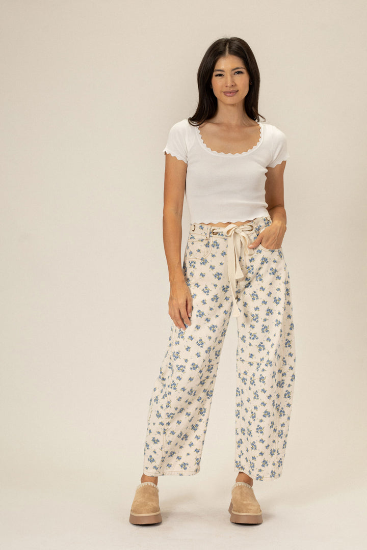 Woman wearing white scoop-neck top and beige floral print wide-leg pants, posing against a neutral background.