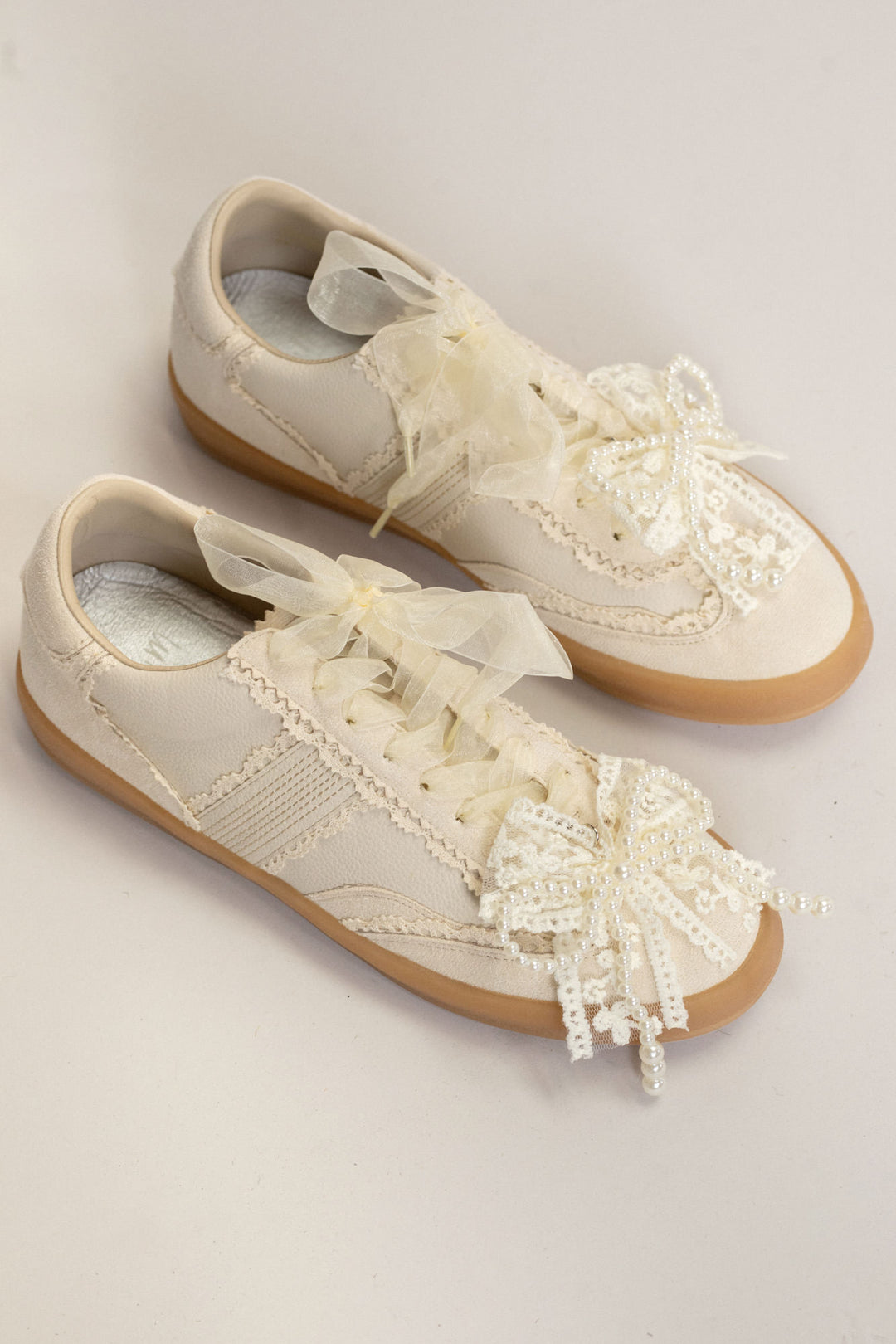 Beige sneakers with lace trim, tulle bows, and gum soles - stylish and feminine footwear.