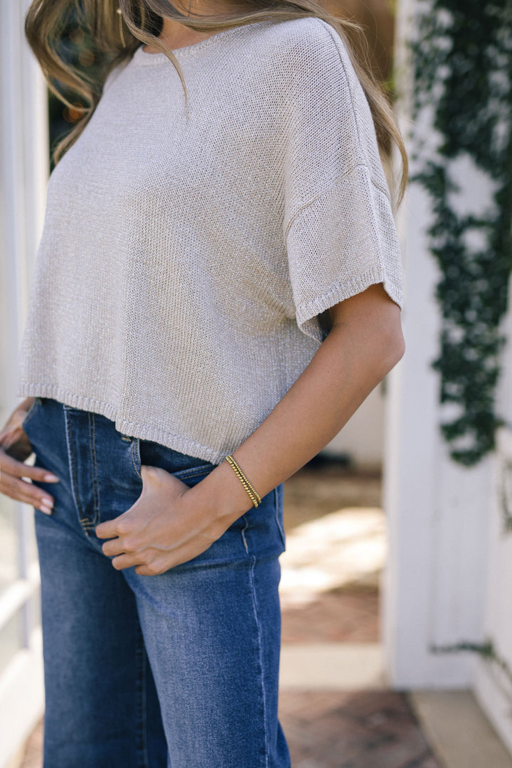 Soft gray knit top with short sleeves and a relaxed, slightly oversized fit, modeled by a woman wearing fitted blue jeans.