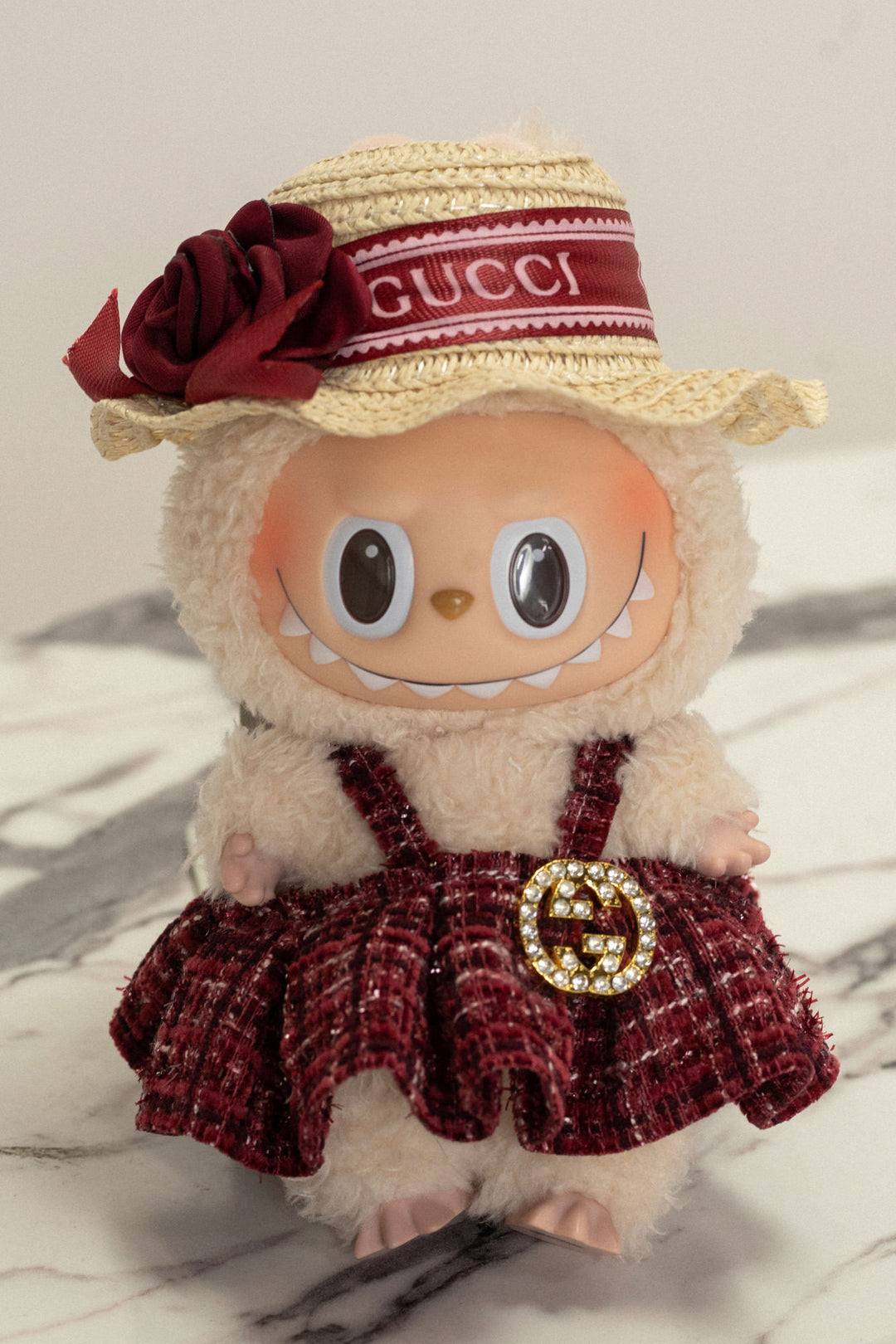Plush white Labubu figure wearing a burgundy tweed dress with Gucci logo band and matching straw hat with red rose.