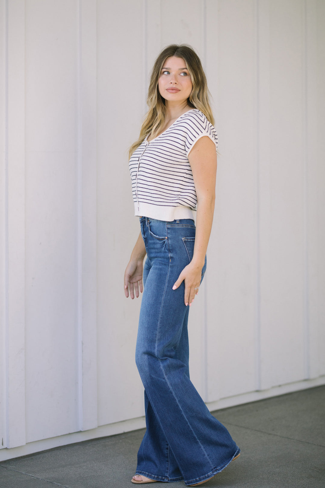 Woman wearing striped top and wide-leg denim jeans, standing against a white wall.