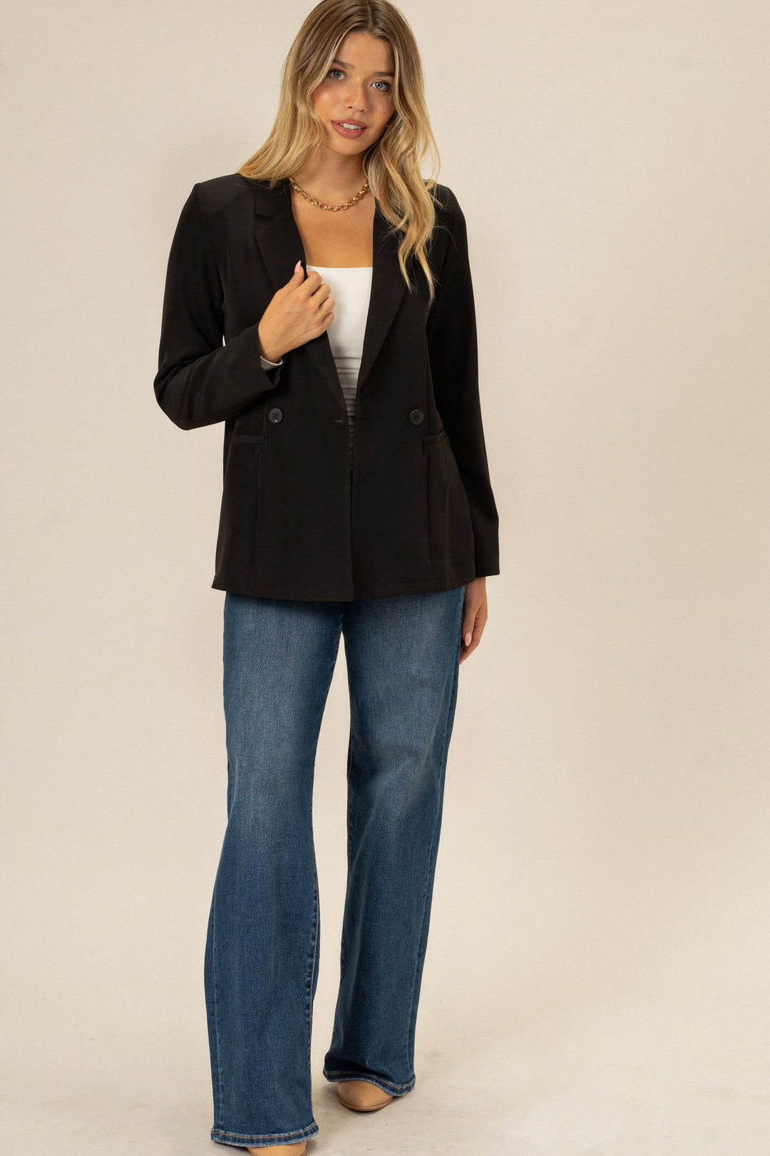 A young woman with long, wavy blonde hair models a classic black double-breasted blazer with a slim fit and button detail.