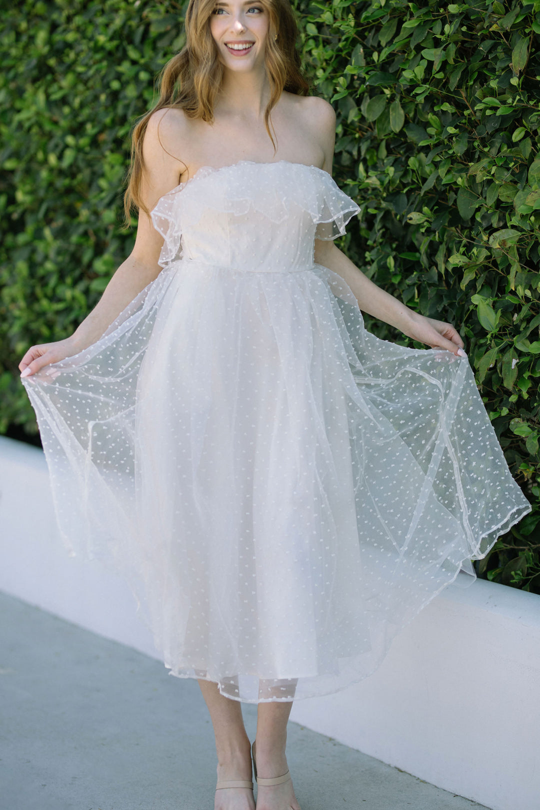 A flowing white tulle midi dress with an off-the-shoulder ruffled neckline, dotted with white polka dots, creating a whimsical, romantic look.