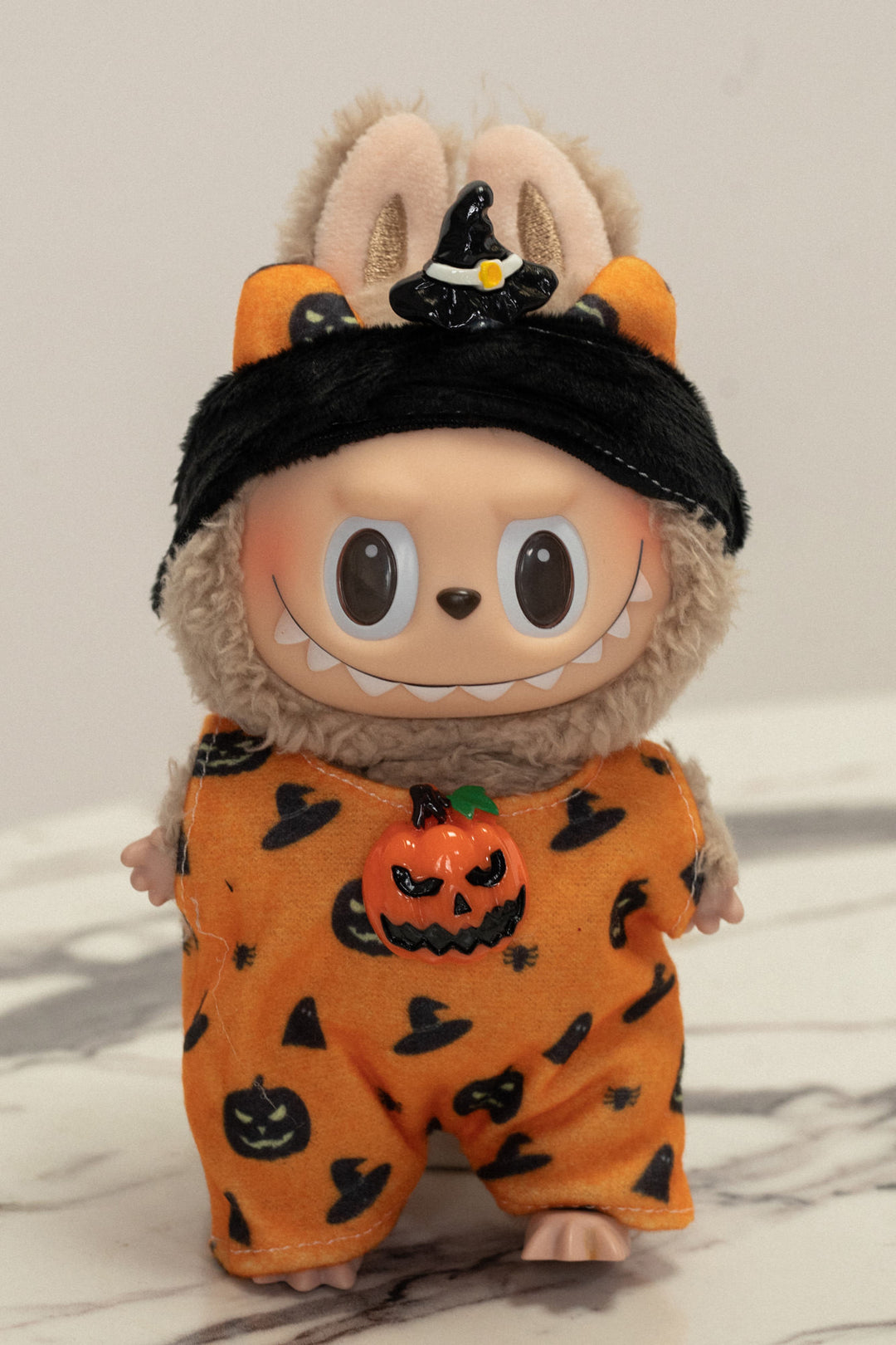 Plush Halloween cat-eared figure in orange pumpkin-patterned costume with black witch hat and large eyes.