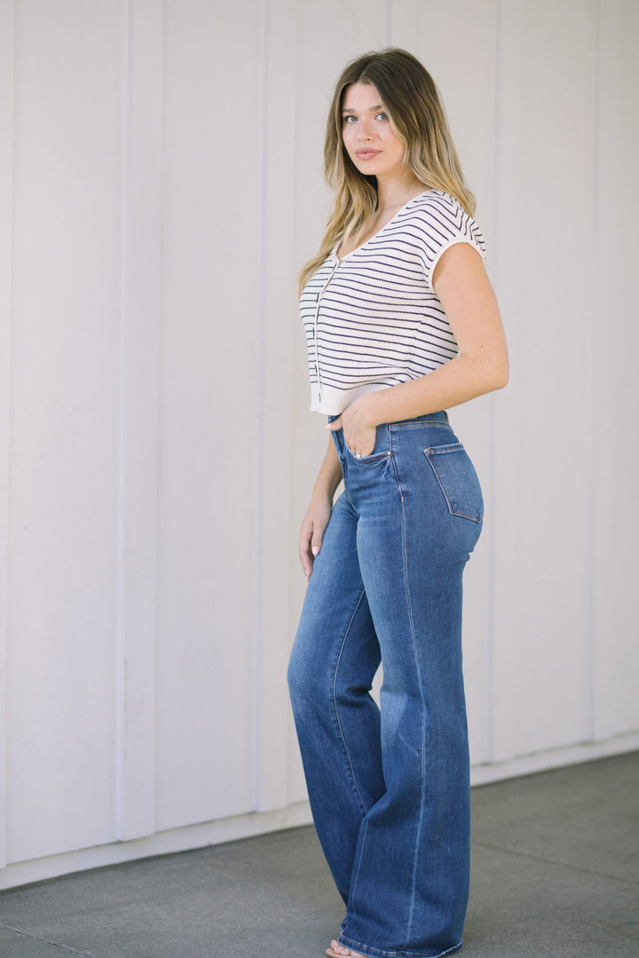 A young woman wearing a striped top and wide-leg denim jeans, standing against a white background.