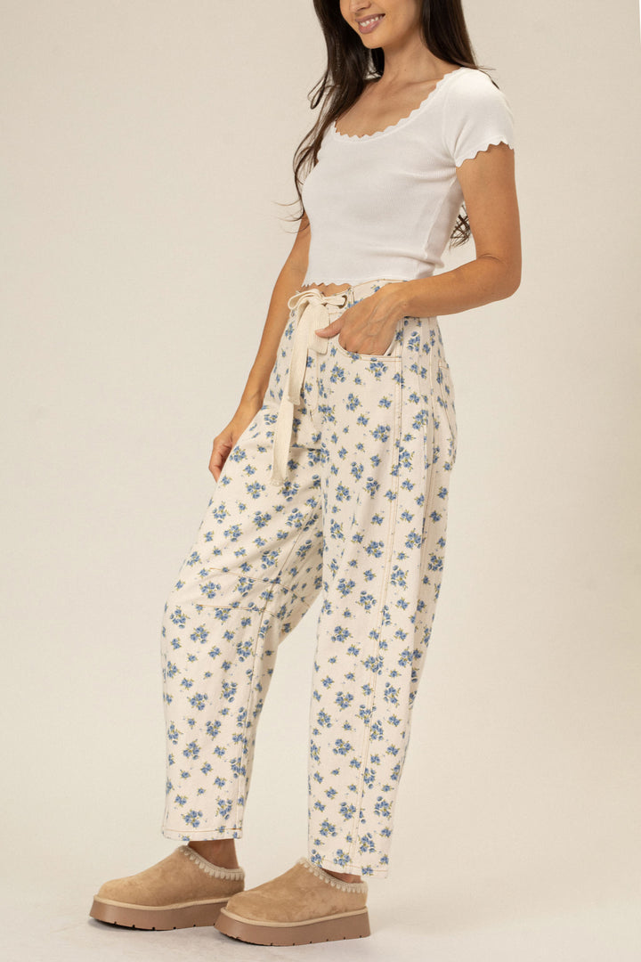 A woman wearing white ribbed top and floral printed barrel pants with a cinched waist and long length, paired with beige platform sandals.