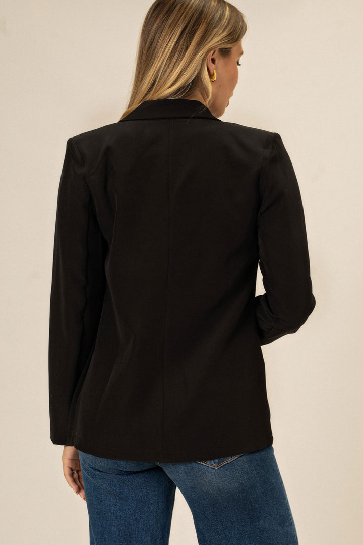 A black, double-breasted blazer with notched lapels, worn by a model with shoulder-length blonde hair.
