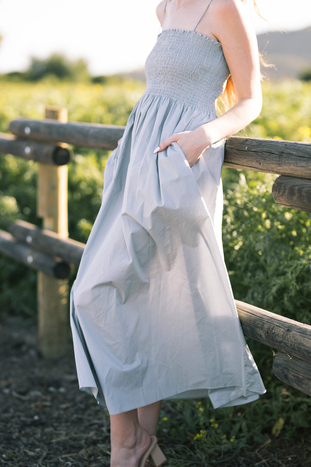 A flowing gray maxi dress with a smocked bodice and pockets, shown in a natural outdoor setting.