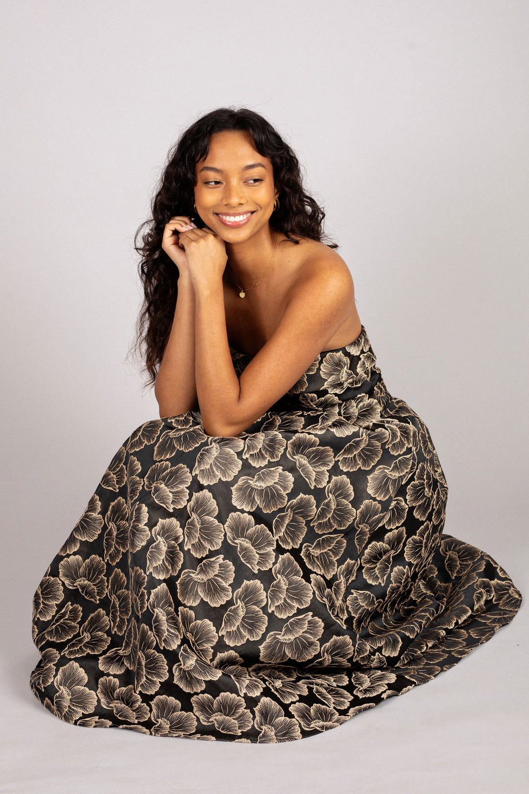 A woman wearing a strapless jacquard dress with a bold floral print in dark and light tones, smiling confidently.