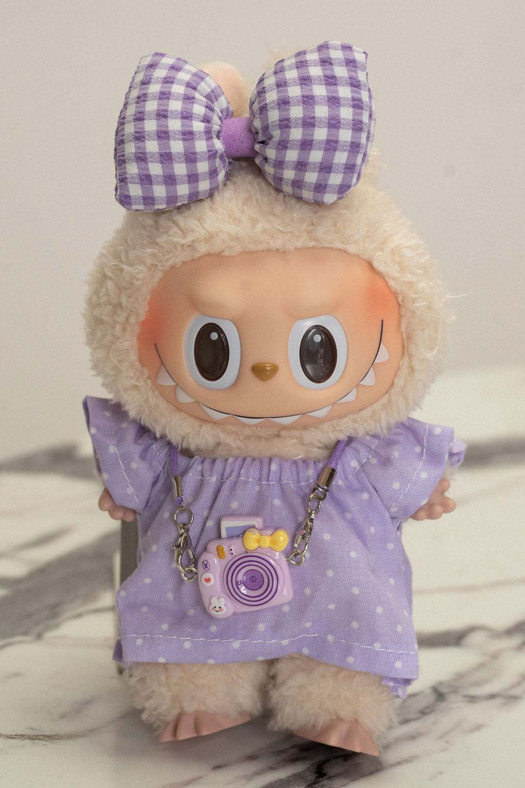 Plush toy with large purple bow and checkered shirt, featuring a camera-shaped accessory.