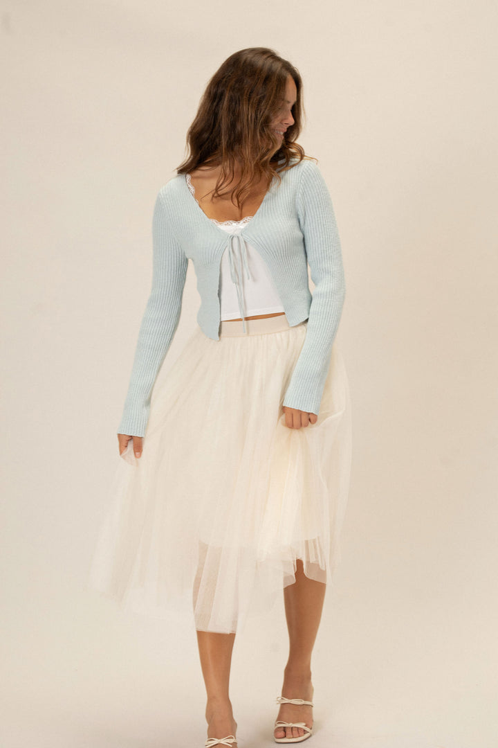 Light blue ribbed cropped top with a tie front detail, paired with a white tulle midi skirt and sandals.