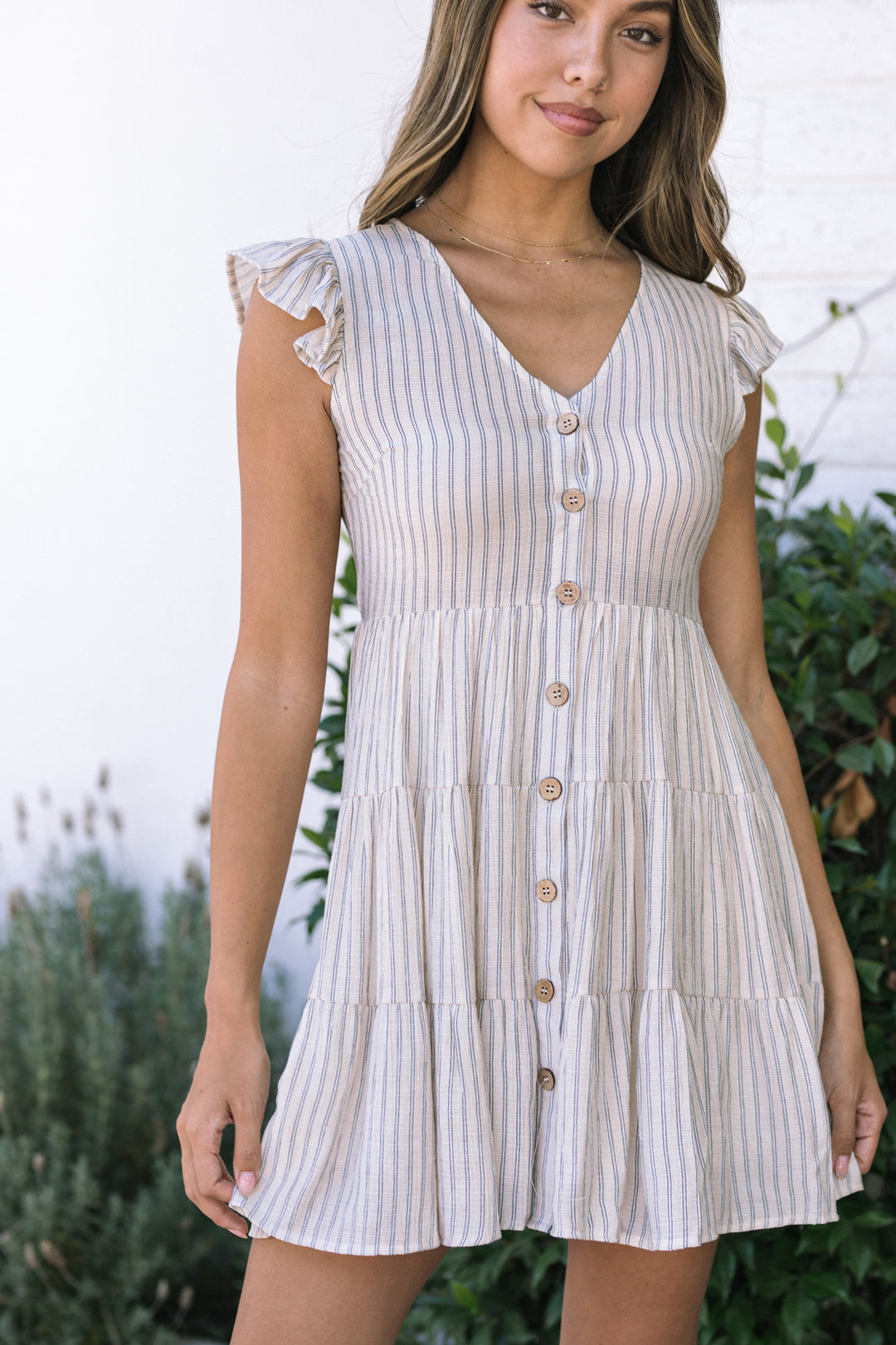 A light gray and white striped, tiered mini dress with ruffled sleeves and decorative buttons down the front.